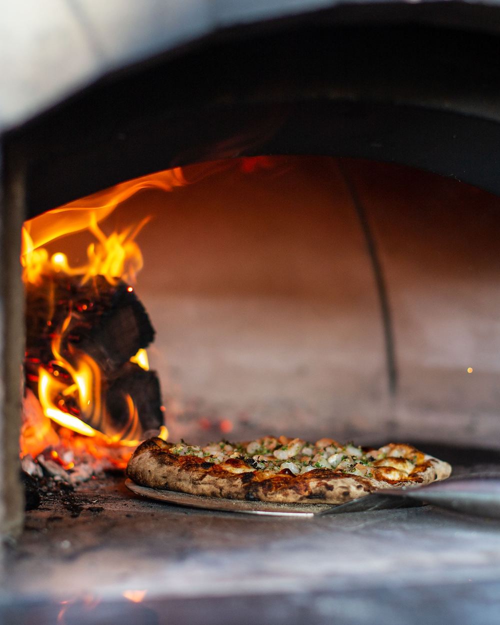 Una pizza dins del forn de llenya, al costat del foc
