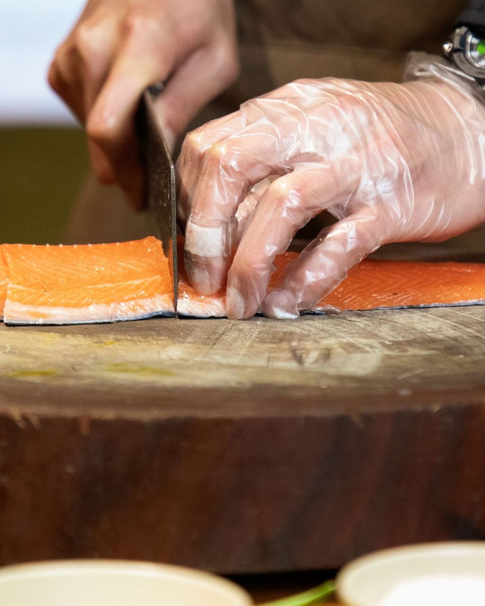 Unes mans amb guants tallen un filet de salmó sobre un tall de fusta